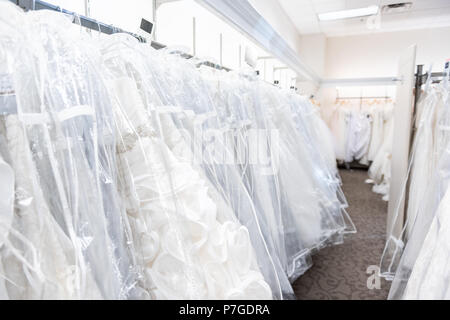 Many wedding dresses gowns in boutique discount store, white garments hanging on rack hangers row closeup with white lace, tulle, design Stock Photo