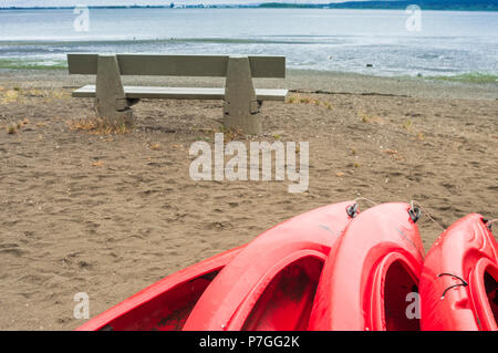 Empty red plastic recreational kayaks for rent or hire, stored on sandy beach on a rainy day.  Crescent Beach, Surrey, British Columbia, Canada. Stock Photo