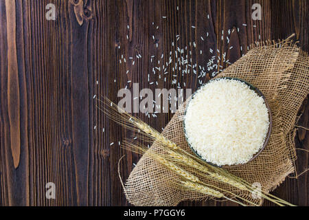 White rice in bowl and ear of paddy on wooden table. Stock Photo