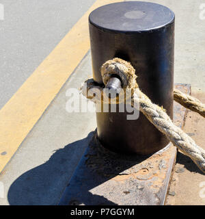 Bollard on a rusty iron plate with a weathered thick rope of hemp, port of Hamburg Stock Photo
