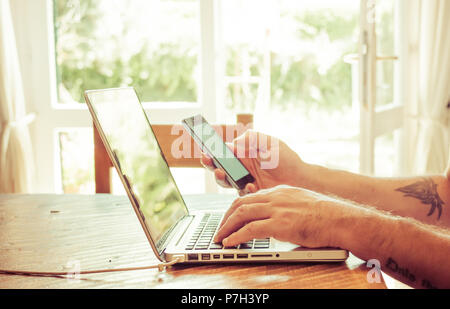 male hands texting on smartphone while working on laptop Stock Photo