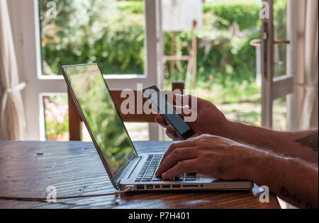 male hands texting on smartphone while working on laptop Stock Photo