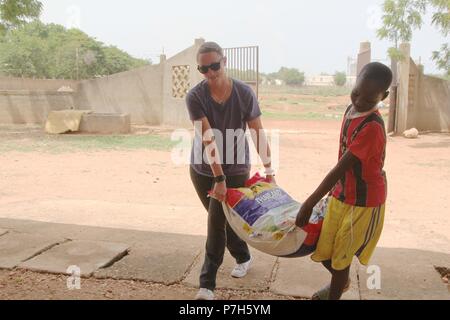 TSgt Chasity Castonguay, a Task Force Darby airman, helps a young boy from the Saare Jabbaama children’s home carry a bag of rice donated by U.S. citizens near Garoua, Cameron June 28, 2018. TF Darby service members are serving in a support role for the Cameroonian Military’s fight against the violent extremist organization Boko Haram. Stock Photo