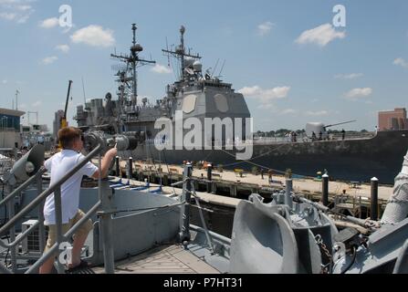 A visitor on-board the USS Wisconsin (BB-64) has a rare opportunity to watch the USS Monterey (CG-61) dock next to the museum ship. The Monterey will be docked behind the Hampton Roads Naval Museum and Nauticus at the Half-Moon cruise ship terminal through July 4, 2018. The Ship's crew will host free tours to the general public starting at 10am through 4pm on July 4, 2018.     The Hampton Roads Naval Museum is one of ten Navy museums that are operated by the Naval History & Heritage Command. It celebrates the long history of the U.S. Navy in the Hampton Roads region of Virginia and is co-locat Stock Photo