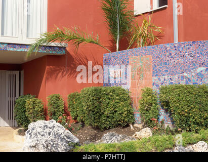Clipped shrubs in front of blue mosaic panel on wall of terracotta-coloured coastal house Stock Photo