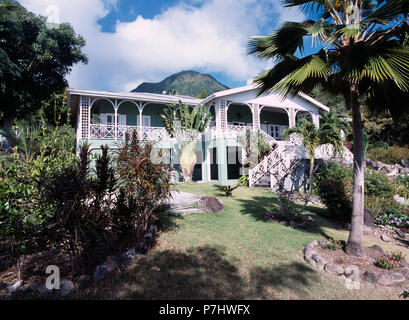 Palm trees and exotic shrubs in garden in front of traditional Caribbean house with balconies and veranda Stock Photo