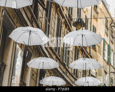 Multicolored, bright umbrellas hanging between houses on the beautiful, narrow streets of the magnificent city of Genoa against the blue sky, on a sun Stock Photo