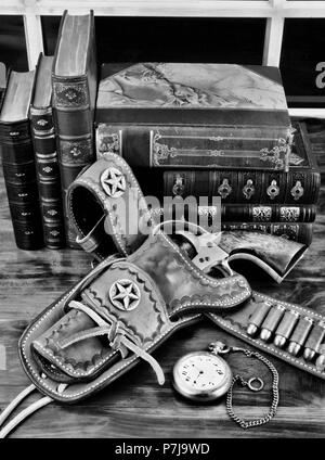 Old cowboy gun in holster with pocket watch and literature in black and white. Stock Photo