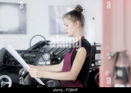 Woman standing by a printing press holding a piece of paper Stock Photo