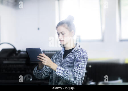 Woman standing in a workshop using a digital tablet Stock Photo