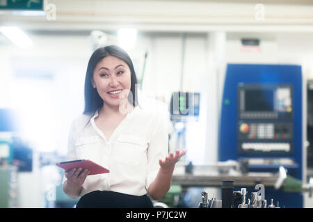 Smiling female engineer standing in a workshop holding a digital tablet Stock Photo