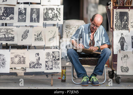 A Cuban artist works on his prints at an outdoor market in Havana. Stock Photo