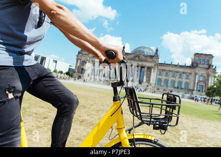 closeup of a young caucasian man riding a bike by the Platz der Republik square, in Berlin, Germany, with the Reichstag building in the background Stock Photo