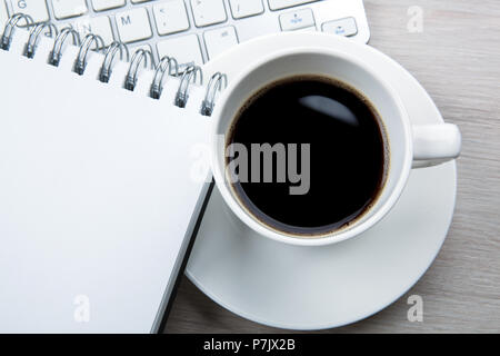 white cup of black coffee with foam, notepad, keyboard on the desktop close up Stock Photo