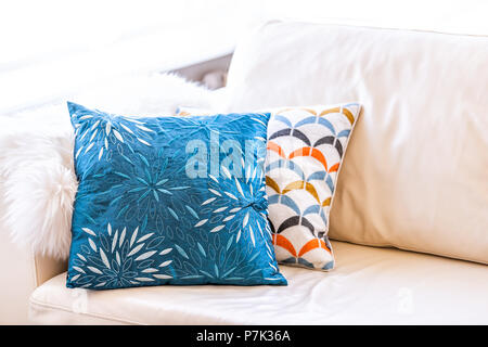 Closeup of two blue and orange pillows on couch or sofa by bright window in modern apartment, house or home with staging of large beige, neutral white Stock Photo