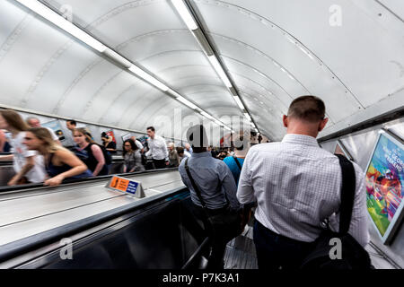London, UK - June 26, 2018: Men riding escalator walking down standing in Underground tube metro during morning commute in center of downtown city in  Stock Photo