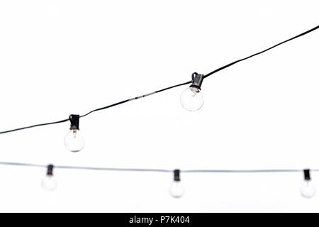 Many hanging light bulbs isolated against white, cloudy overcast sky or studio in outdoor rooftop restaurant closeup Stock Photo