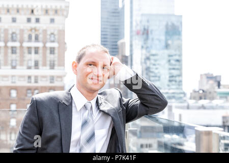 Handsome, attractive young happy smiling businessman closeup face portrait standing in suit, tie, by New York City cityscape skyline in Manhattan afte Stock Photo