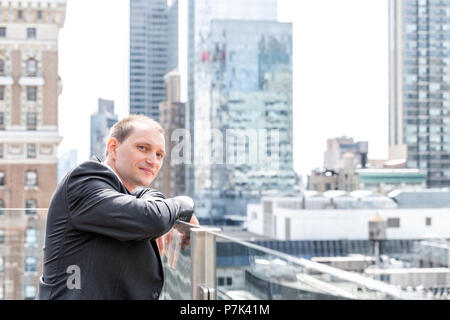 Young businessman portrait standing in suit, tie, looking at New York City cityscape skyline in Manhattan at skyscrapers rooftop happy smiling Stock Photo