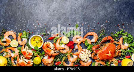 Fresh raw seafood - shrimps and crabs with herbs and spices on dark gray background. Copy space. Stock Photo