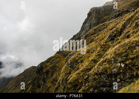 Detail of the side of a rocky mountain with green grass and intense clouds formation on the background. Cool wallpaper image. Peru. South America. No  Stock Photo