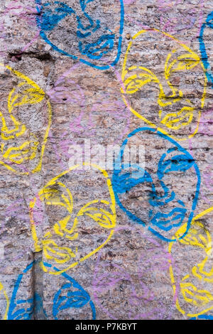 Vertical view of an old worn brick wall covered with cement with blue and yellow graffiti faces painted on it. No people. Stock Photo