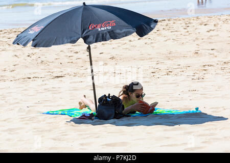 Bournemouth, Dorset, UK. 7th July 2018. UK weather: another hot sunny day as the heatwave continues and thousands of sunseekers head to the  seaside to enjoy the sandy beaches at Bournemouth. Young woman reading a book under the shade of a parasol umbrella. Credit: Carolyn Jenkins/Alamy Live News Stock Photo