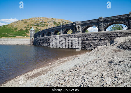 Craig Goch Dam, Wales, UK. 7th July 2018. Extremely low water levels revealing the shoreline due to the current hot weather in the UK, Normally water would be overflowing the arches generating electricity. The Dam normally when full has 2000 million gallons used to supply water to Birmingham along with other dams in the Elan valley. Stock Photo
