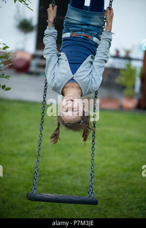 Girl hanging upside down on a swing in the garden Stock Photo