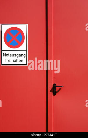 A bright red painted emergency exit on a steel door with a sign. Stock Photo