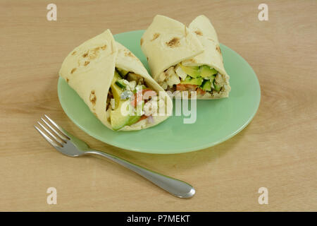 Chicken salad wraps with avocado, cucumber, tomato and feta cheese in tortilla on green plate Stock Photo