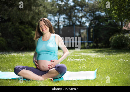Pregnant woman doing fitness exercise on the grass Stock Photo