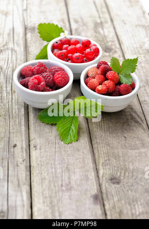 view on three little bowls on a wooden table full of red berries Stock Photo