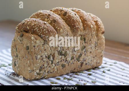 Single loaf of seeded multigrain bread sitting on striped cloth Stock Photo