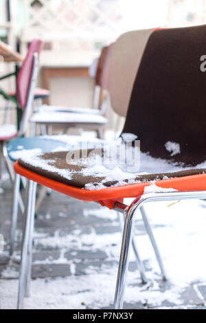 Multi-colored chairs in the snow. Winter in the city. A street cafe in Europe. Travel and tourism. Stock Photo