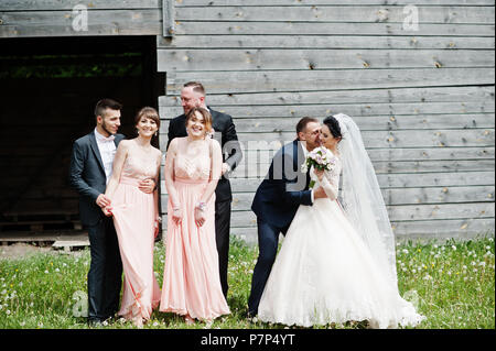 Bridesmaids with groomsmen and wedding couple having fun outdoors next to the old rustic wooden barn. Stock Photo