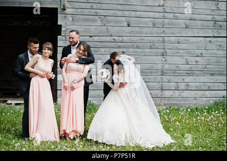 Bridesmaids with groomsmen and wedding couple having fun outdoors next to the old rustic wooden barn. Stock Photo