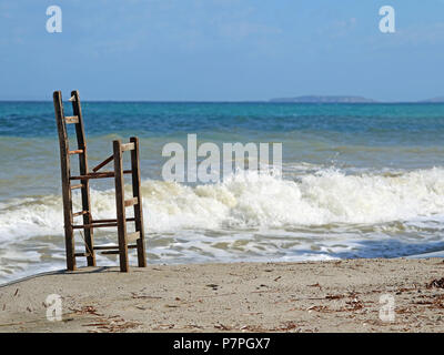 Old broken wooden barstool on the beach and the sea in the background Stock Photo