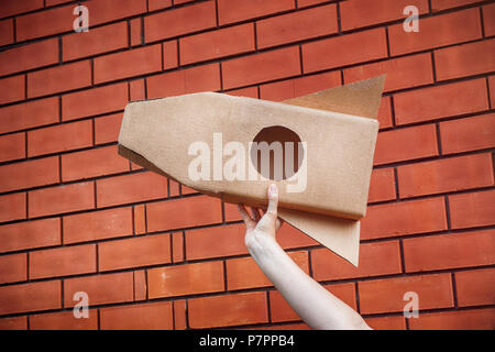 Cardboard space rocket in hand against brick wall. Concept image. Stock Photo
