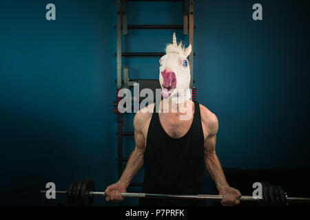 Funny man in comical mask doing sport exercise. Unusual guy pump up iron at home. Unicorn sportsman. Stock Photo