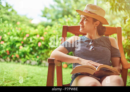 Reading book activity concept. Young hispanic woman with book in hand sitting at summer terrace Stock Photo