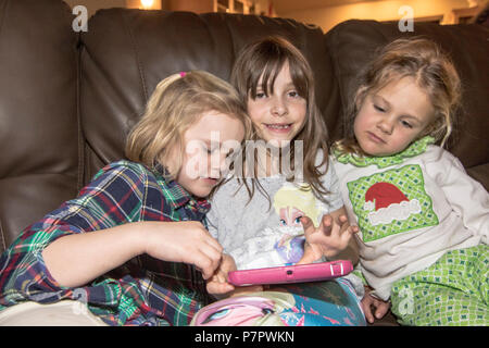 Three pretty, girl cousins,  playing with tablet, cuddled  on chair. Cranbrook, BC, Canada. Modlel released- left to right-#113, #104, #114 Stock Photo