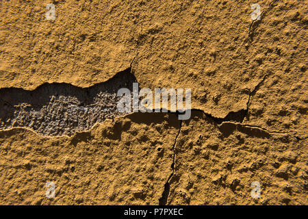 Yellow peeling paint on a grey cracked concrete wall. Stock Photo