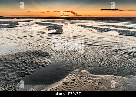 Orange sunrise light on the mouth of the Somme River. The sky is reflected in the puddles of the low tide Stock Photo