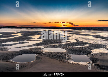 Orange sunrise light on the mouth of the Somme River. The sky is reflected in the puddles of the low tide Stock Photo