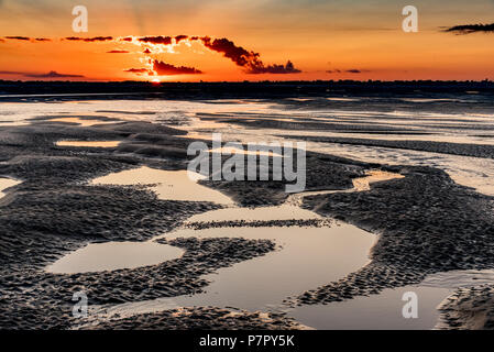 Orange sunrise light on the mouth of the Somme River. The sky is reflected in the puddles of the low tide Stock Photo