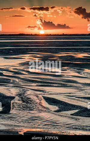 Orange sunrise light on the mouth of the Somme River. The sky is reflected in the puddles of the low tide Stock Photo