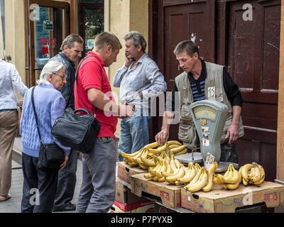 LVIV, UKRAINE - AUGUST 21, 2015: Banana seller on a stand on Lviv market (Rinok) with people buying them. A vintage scale is visible on the foreground Stock Photo