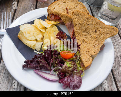 Lunch snack meal on an outside café table roast beef sandwich on brown bread with salad and potato crisps Stock Photo