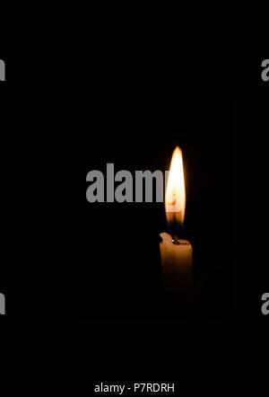 Single burning candle flame glowing brightly against a solid pitch black background with space for text. Stock Photo